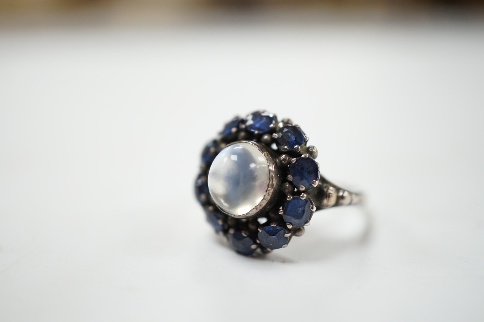An Arts & Crafts white metal, moonstone and sapphire set circular cluster ring, in the manner of Sibyl Dunlop, size M. Condition - fair